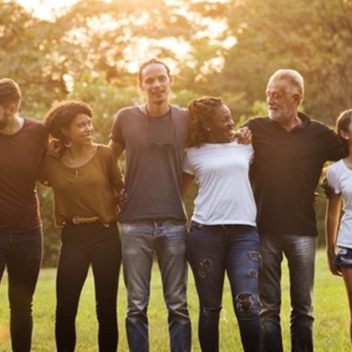 A group of people standing outdoors in a line with their arms around each other, smiling and laughing together